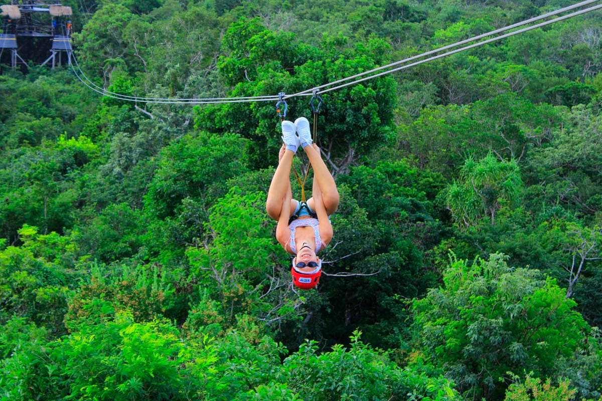 Persona cruzando de cabeza una tirolesa sobre la selva, sujeta del arnés y con la plataforma de salida al fondo.